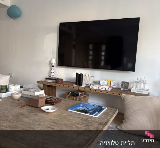חדר מגורים עם טלוויזיה על הקיר ושולחן עץ עם חפצים שונים